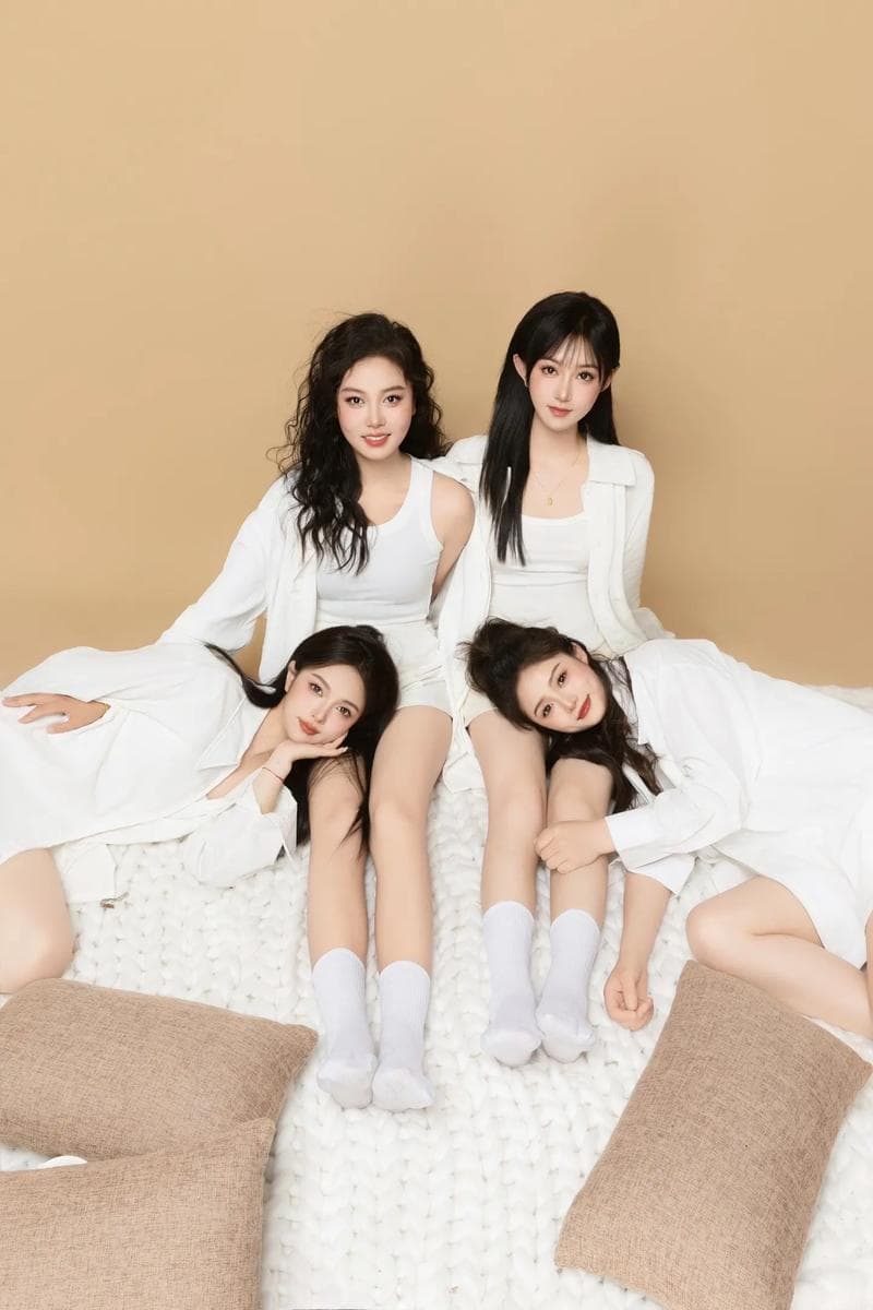 Four young women in matching white outfits pose together on a white textured rug.