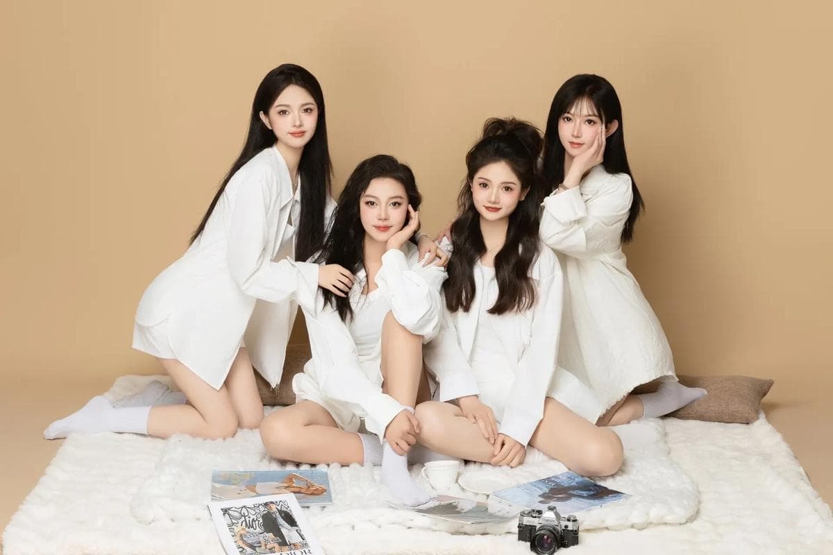 Four young women in white shirts posing on a white rug with magazines and camera.