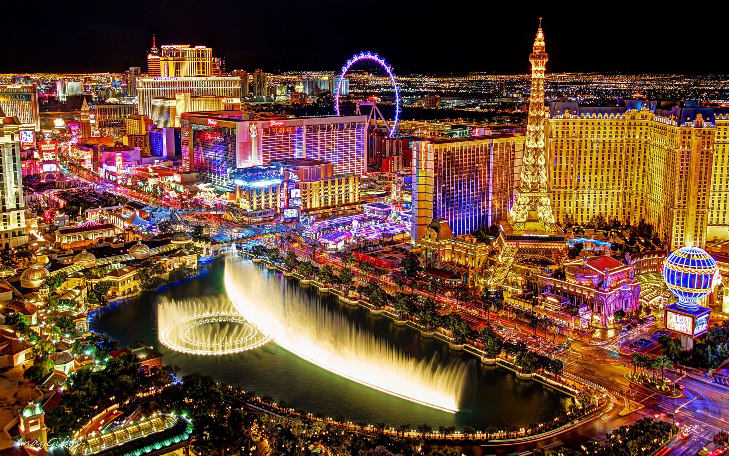 Aerial night view of Las Vegas Strip featuring illuminated Bellagio fountains and Eiffel Tower.